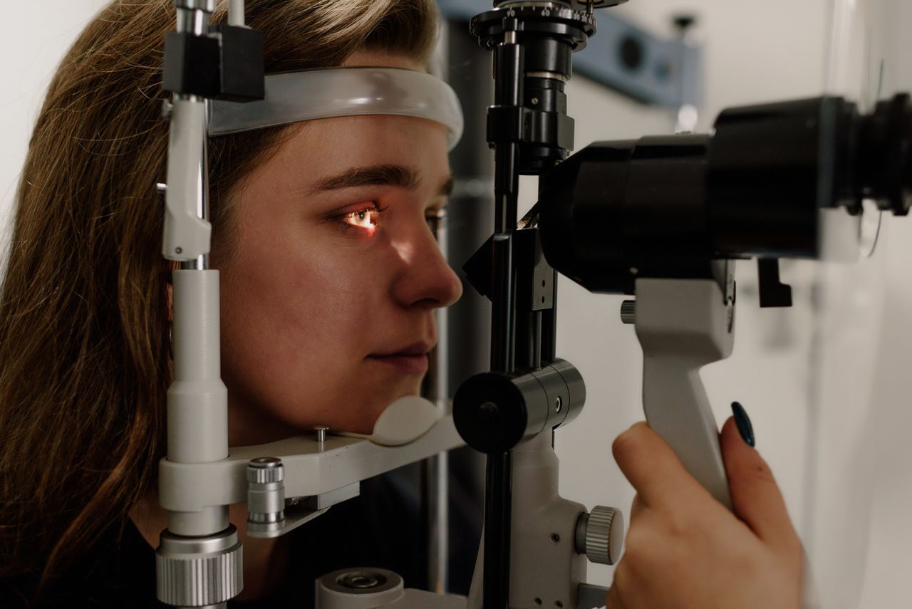 Side view of concentrated female patient looking at light from slit lamp while having eyesight check up in clinic with crop ophthalmologist