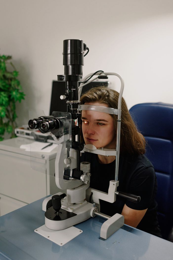 Serious female patient measuring eyesight on professional ophthalmologist equipment in modern clinic during appointment